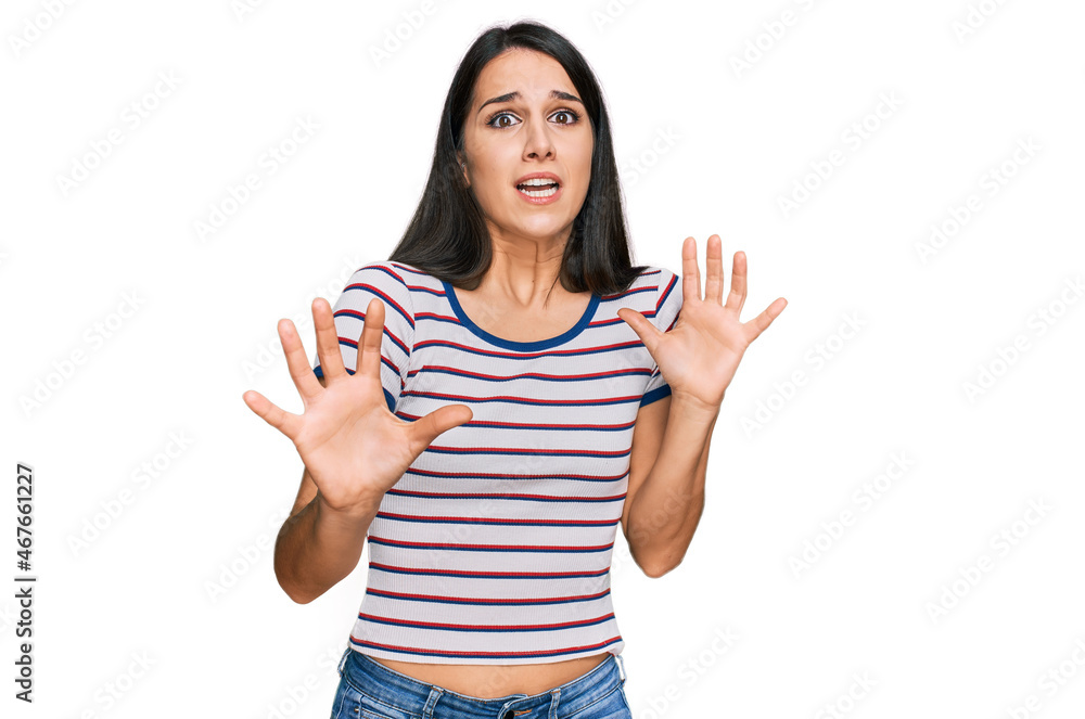 Young hispanic girl wearing casual striped t shirt afraid and terrified with fear expression stop gesture with hands, shouting in shock. panic concept. Young hispanic girl wearing casual striped t shirt afraid and terrified with fear expression stop gesture with hands, shouting in shock. panic concept.