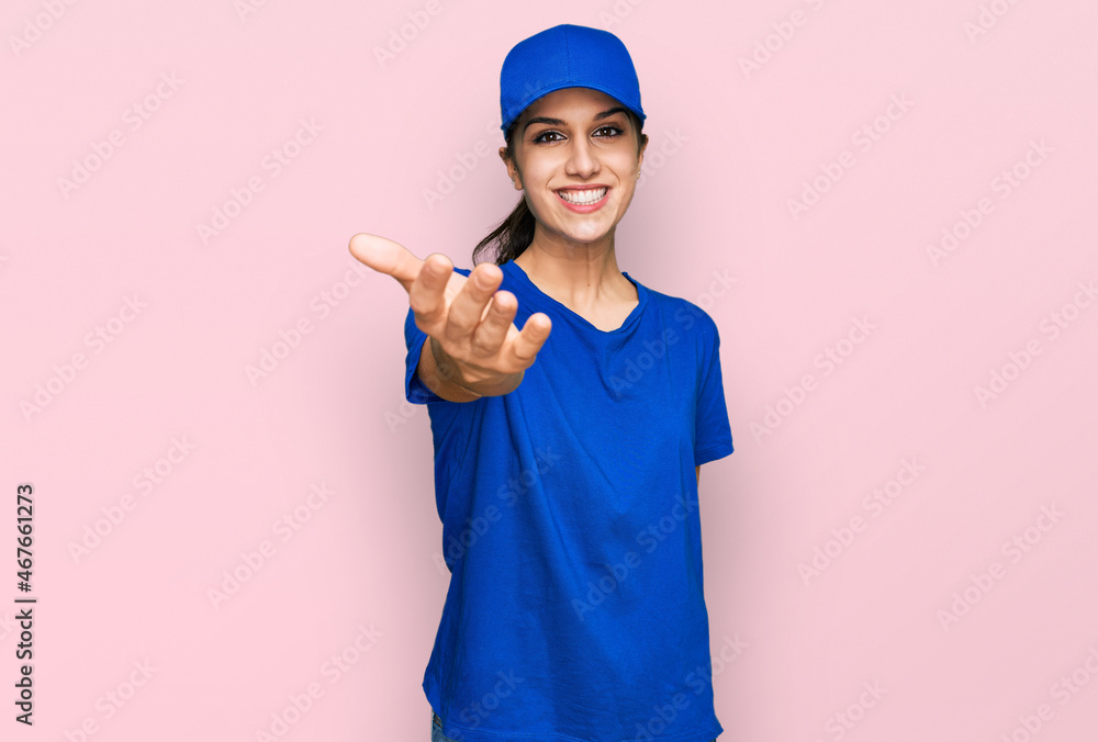 Young hispanic girl wearing delivery courier uniform smiling friendly offering handshake as greeting and welcoming. successful business.