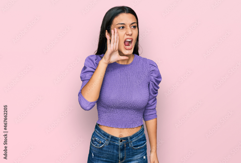 Young hispanic girl wearing casual clothes shouting and screaming loud to side with hand on mouth. communication concept. Young hispanic girl wearing casual clothes shouting and screaming loud to side with hand on mouth. communication concept.