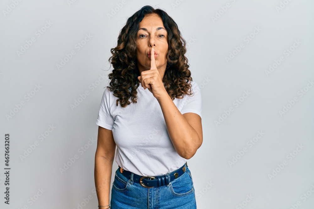 Middle age hispanic woman wearing casual white t shirt asking to be quiet with finger on lips. silence and secret concept. Middle age hispanic woman wearing casual white t shirt asking to be quiet with finger on lips. silence and secret concept.