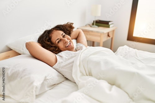Middle age hispanic woman smiling happy lying on the bed at bedroom