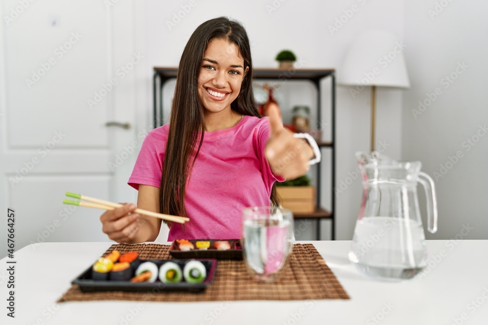 Young brunette woman eating sushi using chopsticks pointing fingers to camera with happy and funny face. good energy and vibes. Young brunette woman eating sushi using chopsticks pointing fingers to camera with happy and funny face. good energy and vibes.