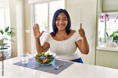 Young hispanic woman eating healthy salad at home showing and pointing up with fingers number six while smiling confident and happy.
