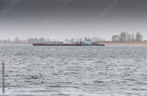 A cargo barge together with a pusher boat go along the Kama River. A barge built by the USSR, the symbol "Hammer and Sickle" on the wheelhouse. A light haze of morning fog over the river.