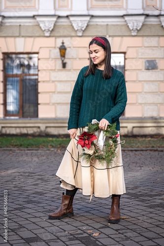 Christmas wreath in the hands of a stylish woman, city walk.