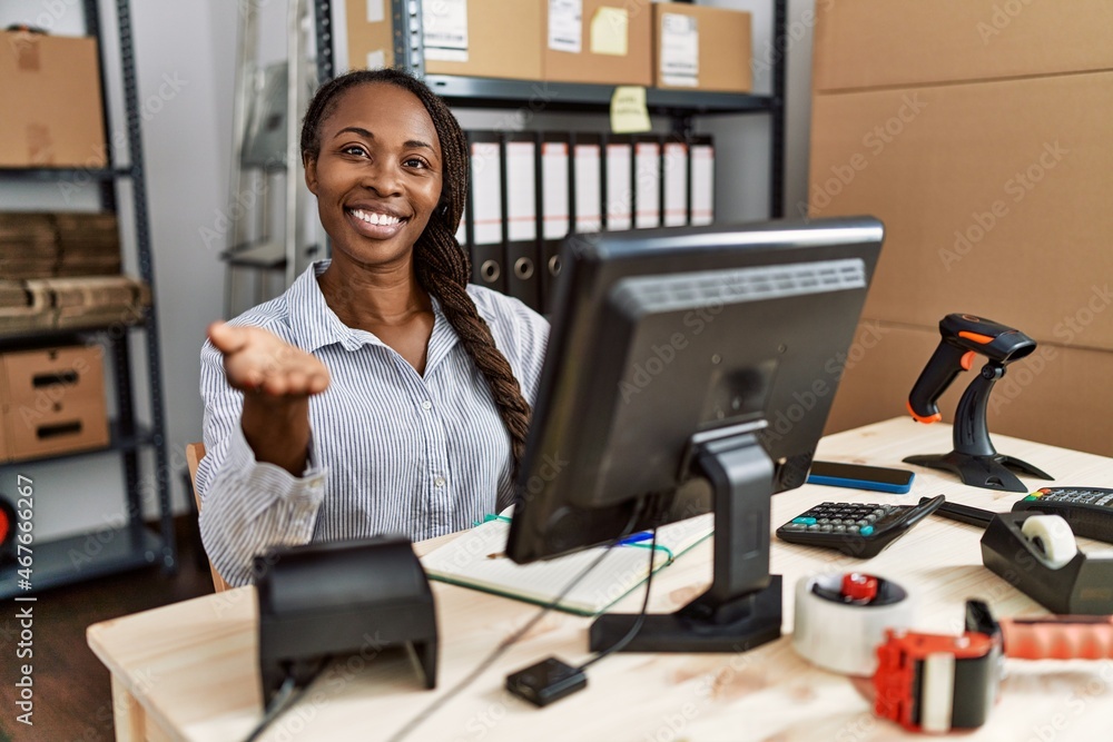 African woman working at small business ecommerce smiling cheerful offering palm hand giving assistance and acceptance. African woman working at small business ecommerce smiling cheerful offering palm hand giving assistance and acceptance.