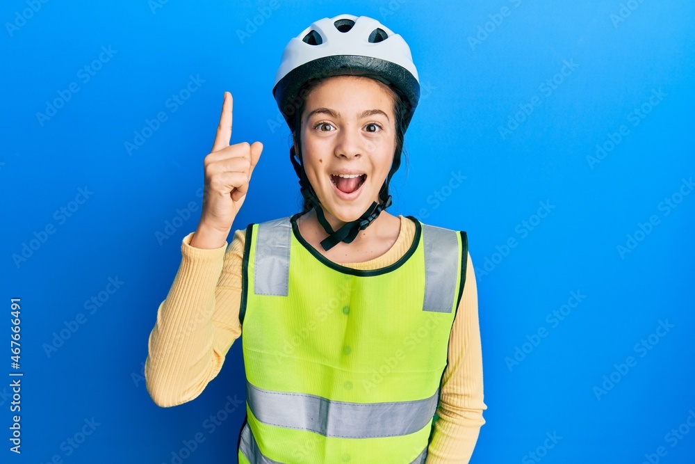 Beautiful brunette little girl wearing bike helmet and reflective vest pointing finger up with successful idea. exited and happy. number one. Beautiful brunette little girl wearing bike helmet and reflective vest pointing finger up with successful idea. exited and happy. number one.