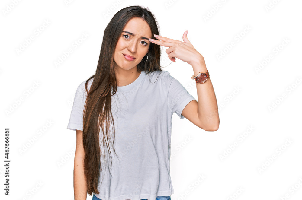 Young hispanic girl wearing casual white t shirt shooting and killing oneself pointing hand and fingers to head like gun, suicide gesture.