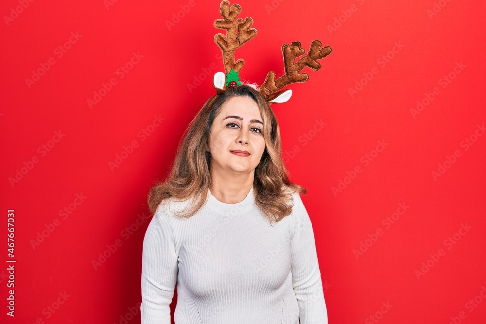 Middle age caucasian woman wearing cute christmas reindeer horns relaxed with serious expression on face. simple and natural looking at the camera. Middle age caucasian woman wearing cute christmas reindeer horns relaxed with serious expression on face. simple and natural looking at the camera.