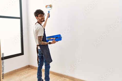 Young hispanic man painting wall using roller at home.