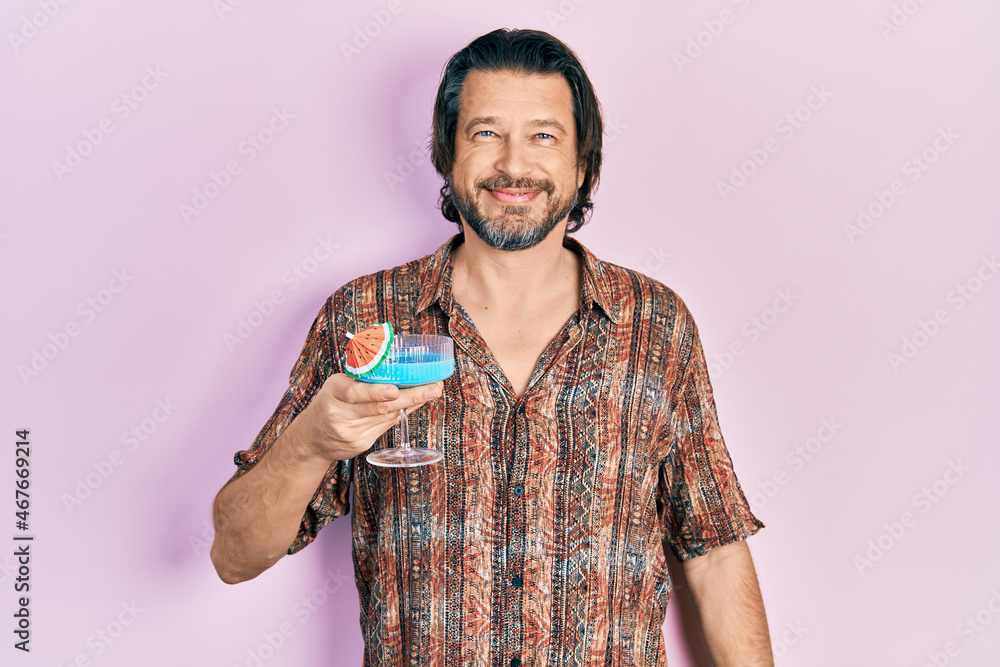 Middle age caucasian man drinking tropical cocktail with alcohol looking positive and happy standing and smiling with a confident smile showing teeth Middle age caucasian man drinking tropical cocktail with alcohol looking positive and happy standing and smiling with a confident smile showing teeth