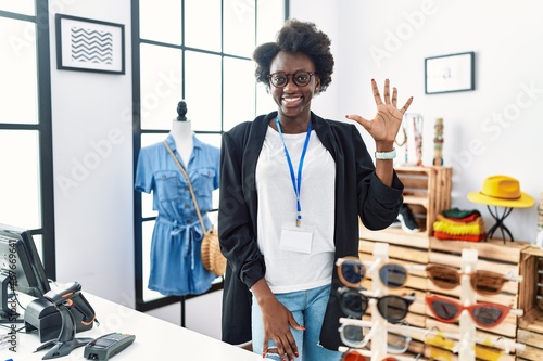 African young woman working as manager at retail boutique showing and pointing up with fingers number five while smiling confident and happy.