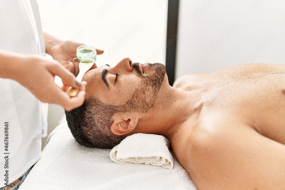 Young hispanic man having facial mask treatment at beauty center Young hispanic man having facial mask treatment at beauty center