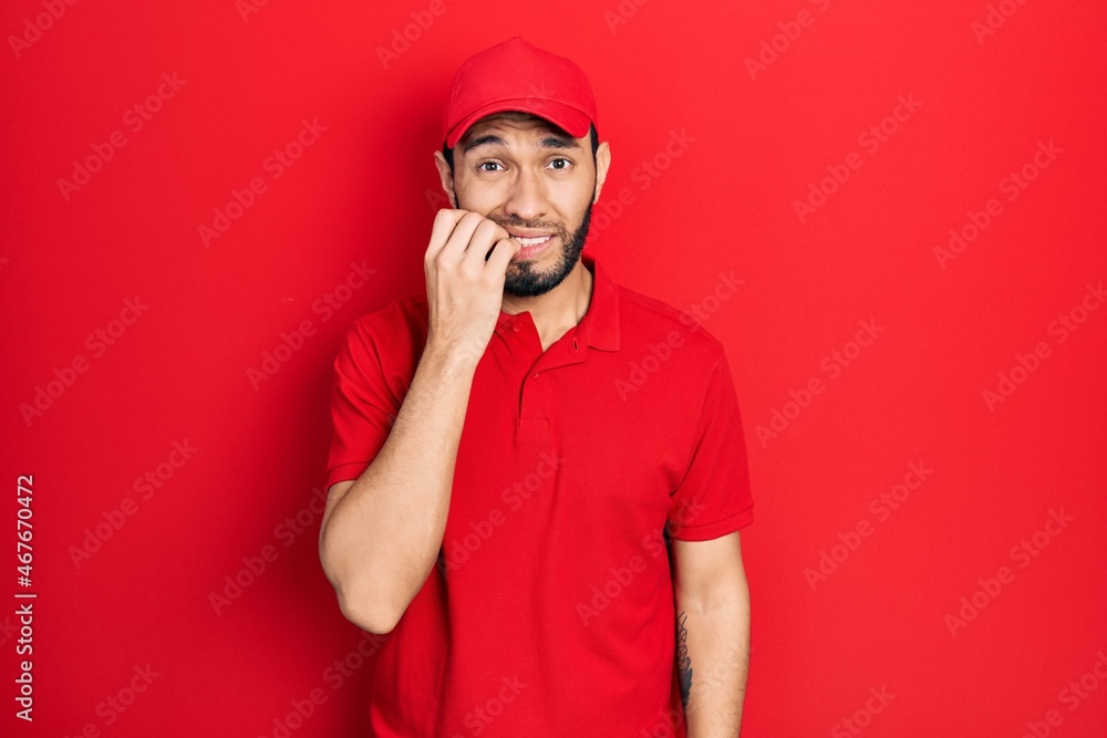 Hispanic man with beard wearing delivery uniform and cap looking stressed and nervous with hands on mouth biting nails. anxiety problem. Hispanic man with beard wearing delivery uniform and cap looking stressed and nervous with hands on mouth biting nails. anxiety problem.