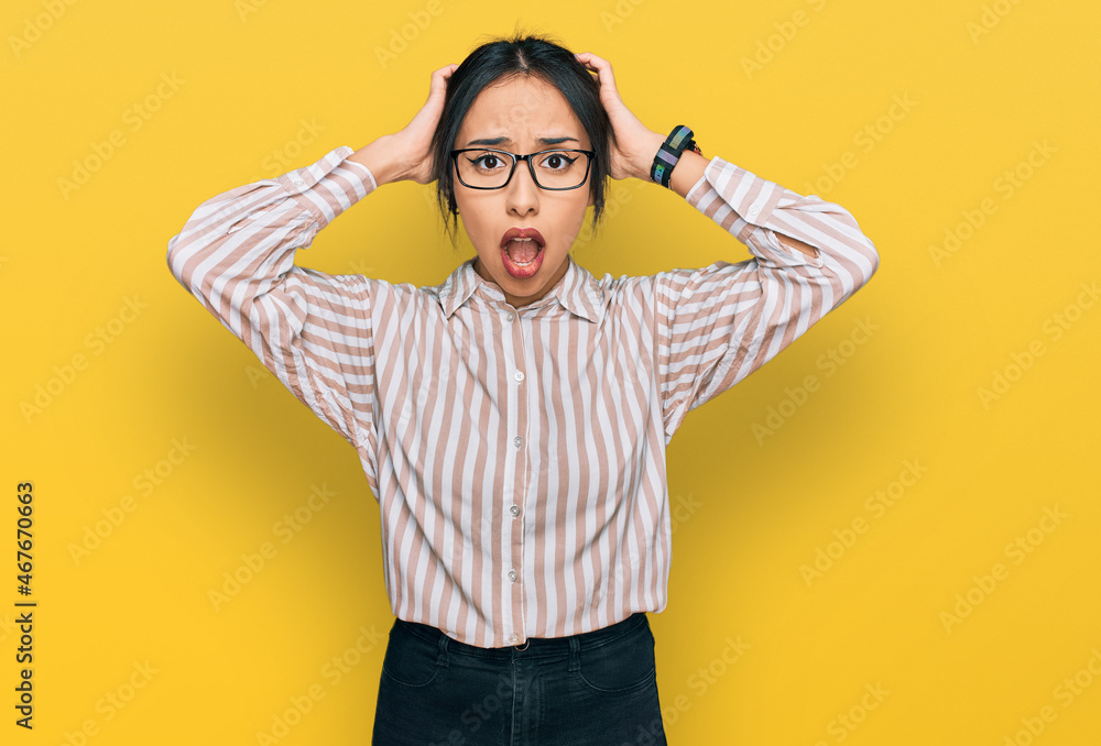 Young hispanic girl wearing casual clothes and glasses crazy and scared with hands on head, afraid and surprised of shock with open mouth Young hispanic girl wearing casual clothes and glasses crazy and scared with hands on head, afraid and surprised of shock with open mouth