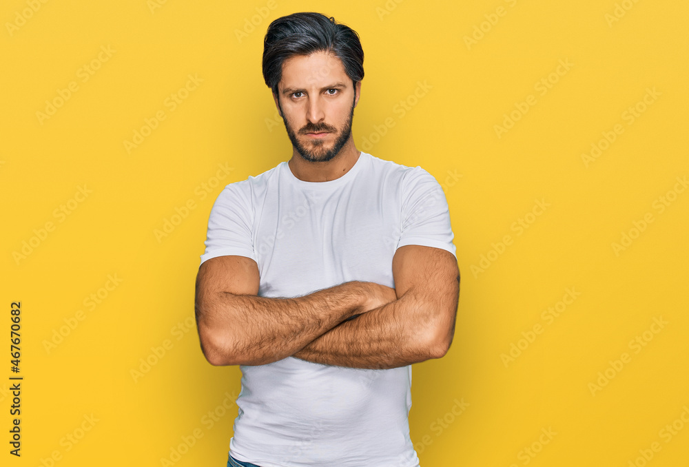 Young hispanic man wearing casual white t shirt skeptic and nervous, disapproving expression on face with crossed arms. negative person. Young hispanic man wearing casual white t shirt skeptic and nervous, disapproving expression on face with crossed arms. negative person.