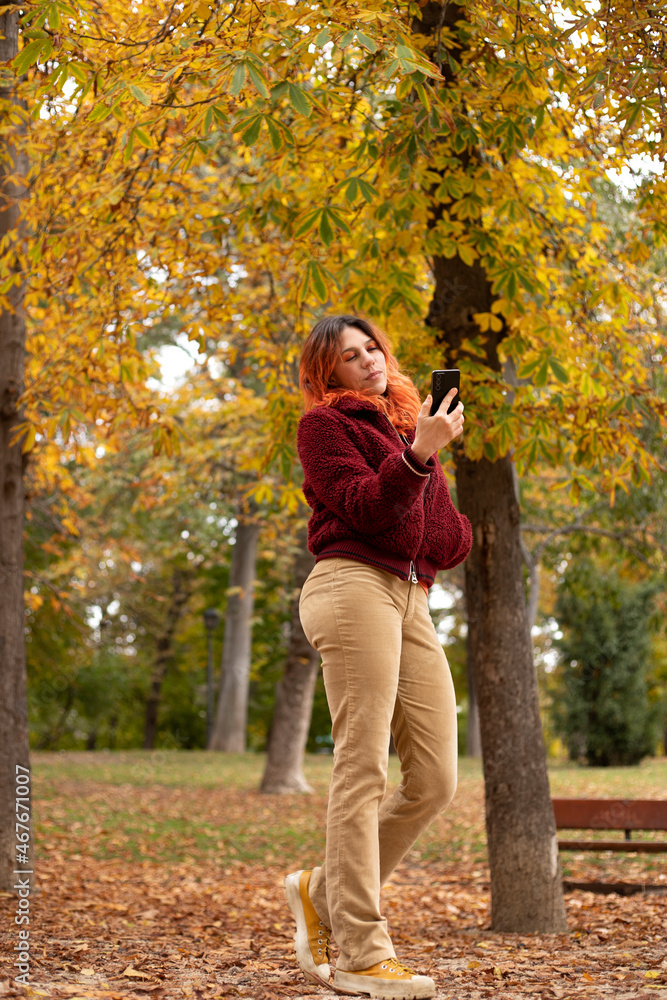 full-body woman with cell phone in hand in a park in autumn full-body woman with cell phone in hand in a park in autumn