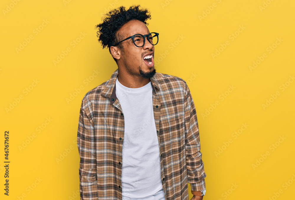 Young african american man with beard wearing casual clothes and glasses angry and mad screaming frustrated and furious, shouting with anger. rage and aggressive concept. Young african american man with beard wearing casual clothes and glasses angry and mad screaming frustrated and furious, shouting with anger. rage and aggressive concept.