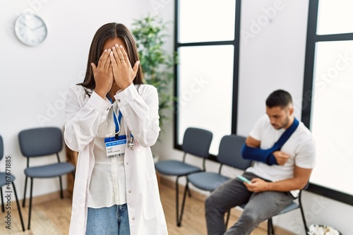 Young asian doctor woman at waiting room with a man with a broken arm with sad expression covering face with hands while crying. depression concept.