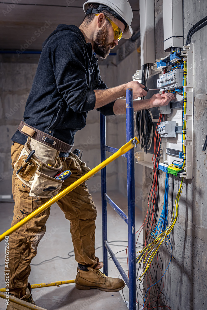 A male electrician works in a switchboard with an electrical connecting cable. A male electrician works in a switchboard with an electrical connecting cable.