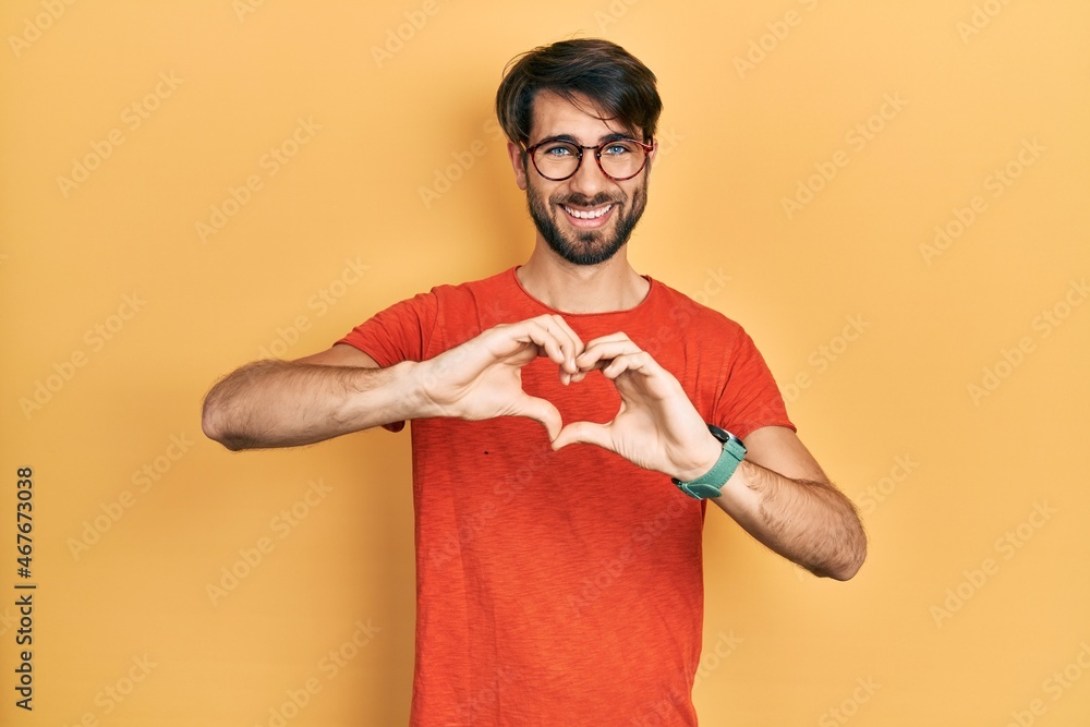 Young hispanic man wearing casual clothes and glasses smiling in love doing heart symbol shape with hands. romantic concept. Young hispanic man wearing casual clothes and glasses smiling in love doing heart symbol shape with hands. romantic concept.