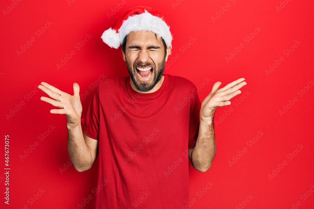 Young hispanic man wearing christmas hat celebrating mad and crazy for success with arms raised and closed eyes screaming excited. winner concept Young hispanic man wearing christmas hat celebrating mad and crazy for success with arms raised and closed eyes screaming excited. winner concept