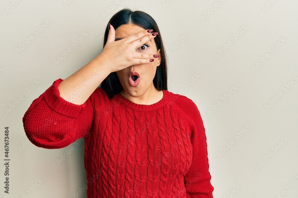Beautiful brunette woman wearing wool winter sweater peeking in shock covering face and eyes with hand, looking through fingers with embarrassed expression. Beautiful brunette woman wearing wool winter sweater peeking in shock covering face and eyes with hand, looking through fingers with embarrassed expression.