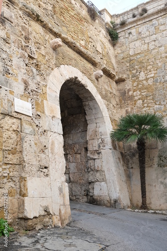 Outdoor venue. Door of the two lions in Cagliari.Ancient limestone walls of the city. Small palm with leaves. Plaque with writing Via Giovanni Spano. Cagliari  Sardinia   Italy.