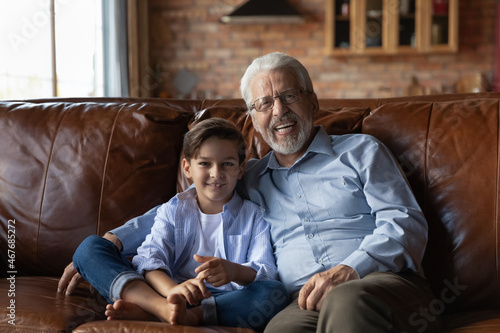 Our future is in offsprings. Home portrait of loving elderly age grandfather and preschool kid grandson cuddle on couch look at camera. Happy old man and little boy relatives have bonding relationship