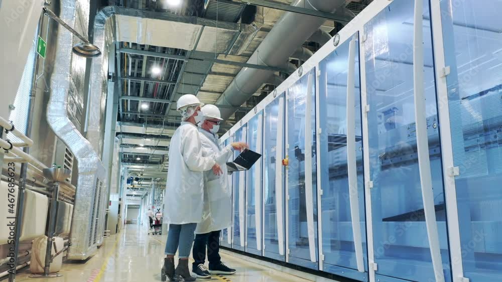 Solar cell factory with two workers observing machines at work Solar cell factory with two workers observing machines at work