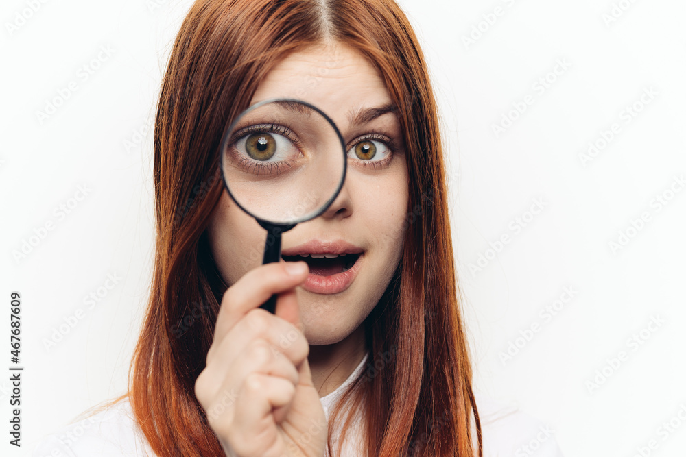 red-haired woman in a white shirt with a magnifying glass in her hands searching red-haired woman in a white shirt with a magnifying glass in her hands searching