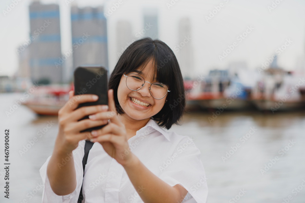 asian teenager toothy smiling while taking a photo by mobile phone