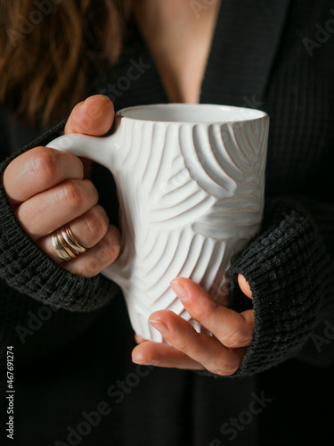 Girl in a black knitted sweater with a white cup in her hands