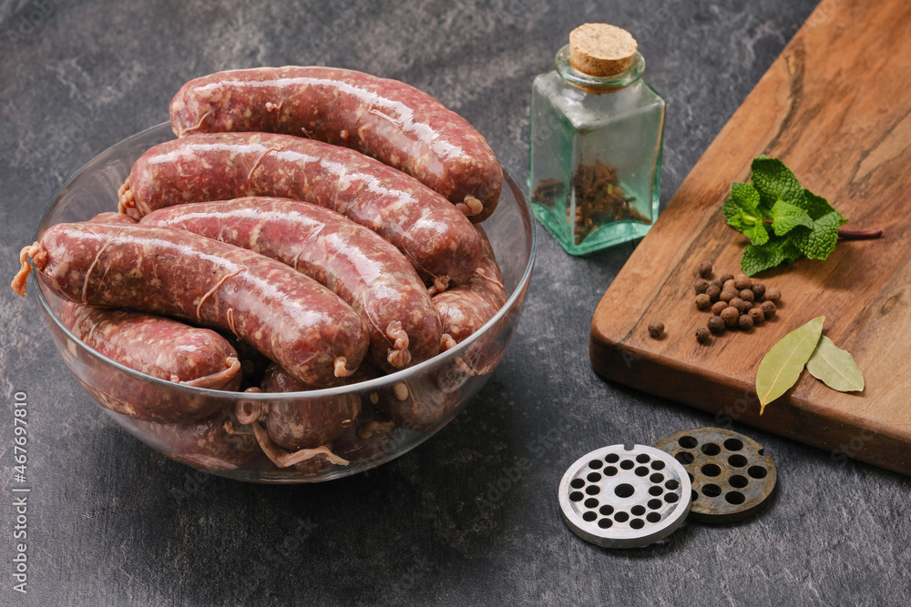 Freshly made raw sausages mix in skins with herbs in a glass bowl. Raw homemade bratwurst sausages with spices, grate, mint from a meat grinder and wooden kitchen board. Focus on wurst Freshly made raw sausages mix in skins with herbs in a glass bowl. Raw homemade bratwurst sausages with spices, grate, mint from a meat grinder and wooden kitchen board. Focus on wurst
