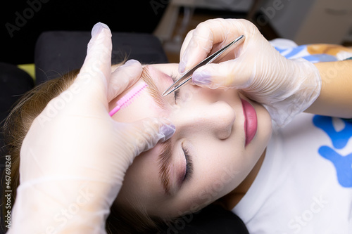 the master s hands in white gloves stretch the eyebrow and pluck out excess eyebrow hairs with tweezers