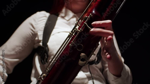 Woman plays bassoon with fingers on keys, closeup, front view. Female musician plays jazz tune in studio on dark background photo