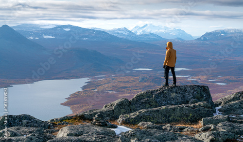 Male hiker overlooking epic view of vast arctic landscape of Stora Sjofallet National Park, Sweden, on autumn day. Mountains and valleys of Lapland. Ahkka massif. View from the top of Lulep Gierkav.