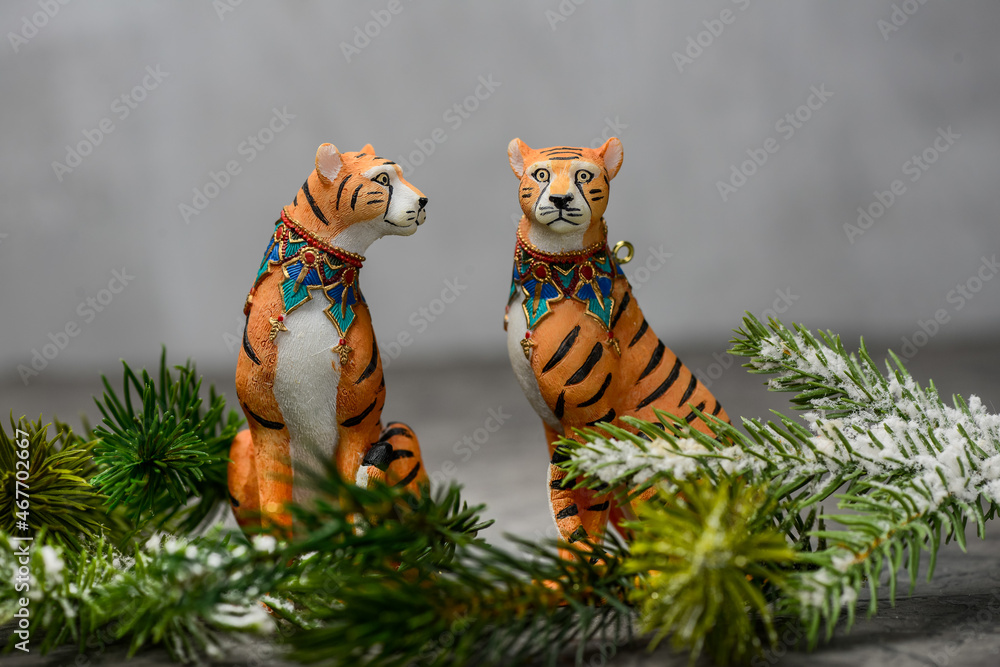 two figurines of tigers on a gray background in fir branches

