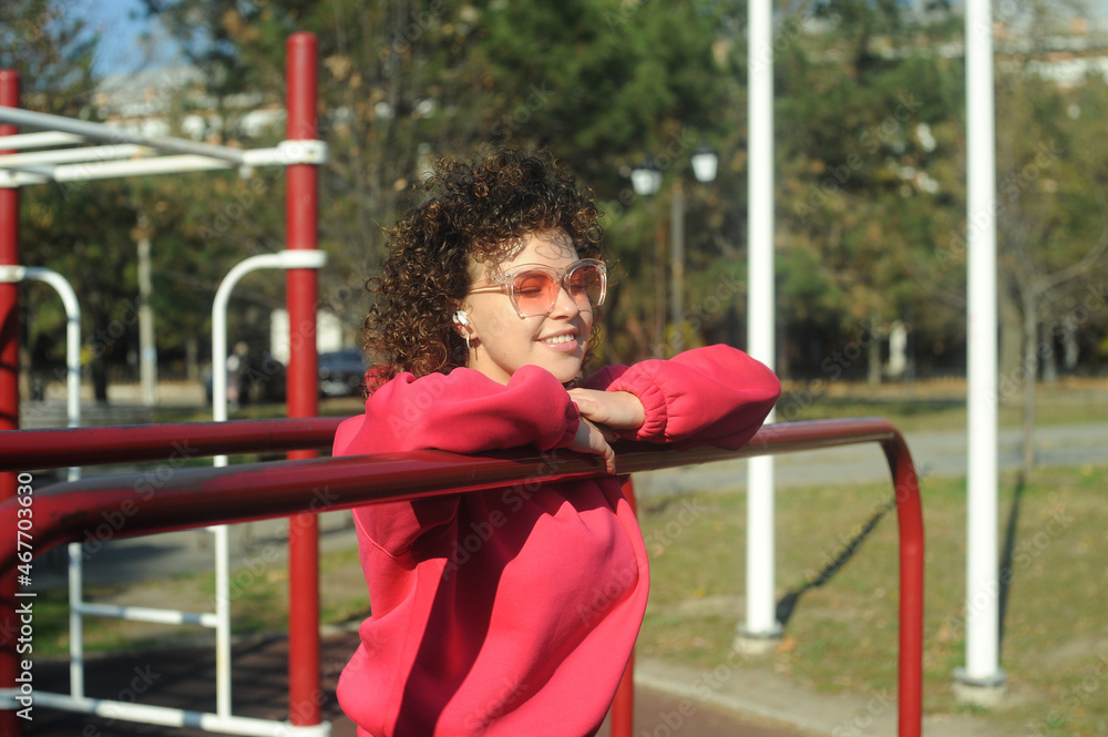 Obraz premium Cute curly hair woman in pink sportswear with headphones on the playground
