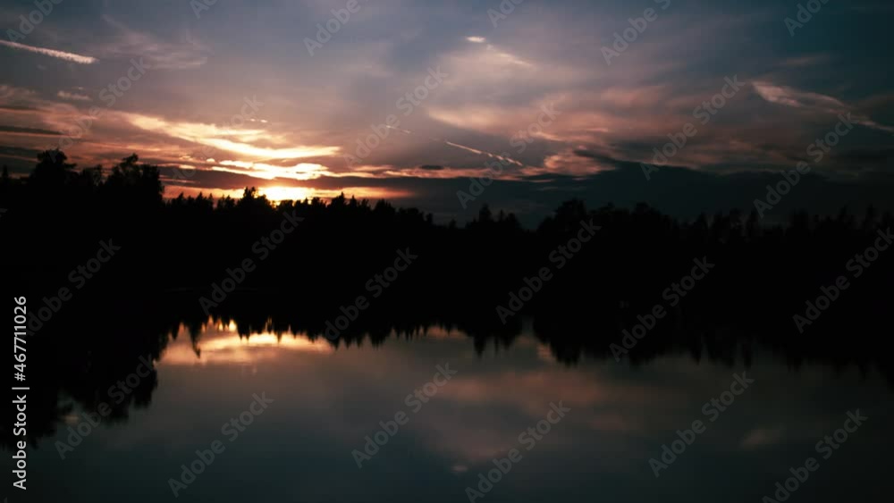 Timelapse - The sinking red sun shines through the treetops in nature. A lake can be seen in which the clouds are reflected. Timelapse - The sinking red sun shines through the treetops in nature. A lake can be seen in which the clouds are reflected.