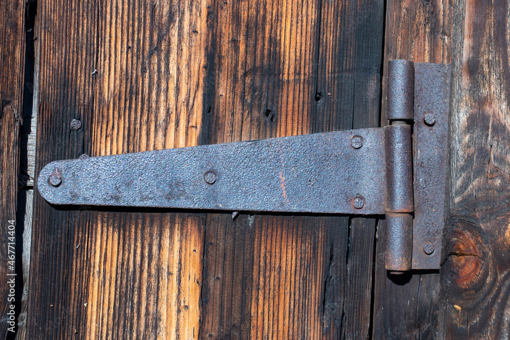 An old metal rusty hinge on a door made of dark old wood. Close-up. Hard daylight.