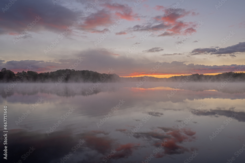Foggy autumn landscape at dawn of the shoreline of Whitford Lake with mirrored reflections in calm water, Fort Custer State Park, Michigan, USA
