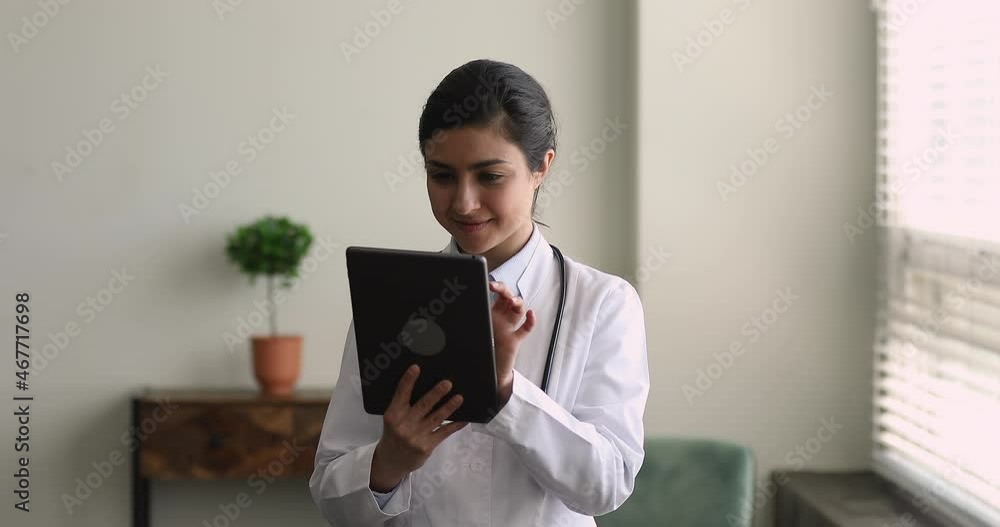 Smiling young beautiful female indian ethnicity doctor general practitioner using digital computer tablet, managing appointments or healthcare treatments, giving distant professional medical help. Smiling young beautiful female indian ethnicity doctor general practitioner using digital computer tablet, managing appointments or healthcare treatments, giving distant professional medical help.
