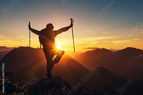 silhouette of hiker person performing yoga posture after summiting on the mountain at sunset.