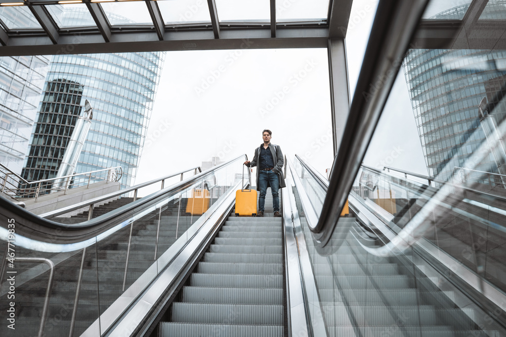 Businessman with baggage getting down on the escalator to the departure area