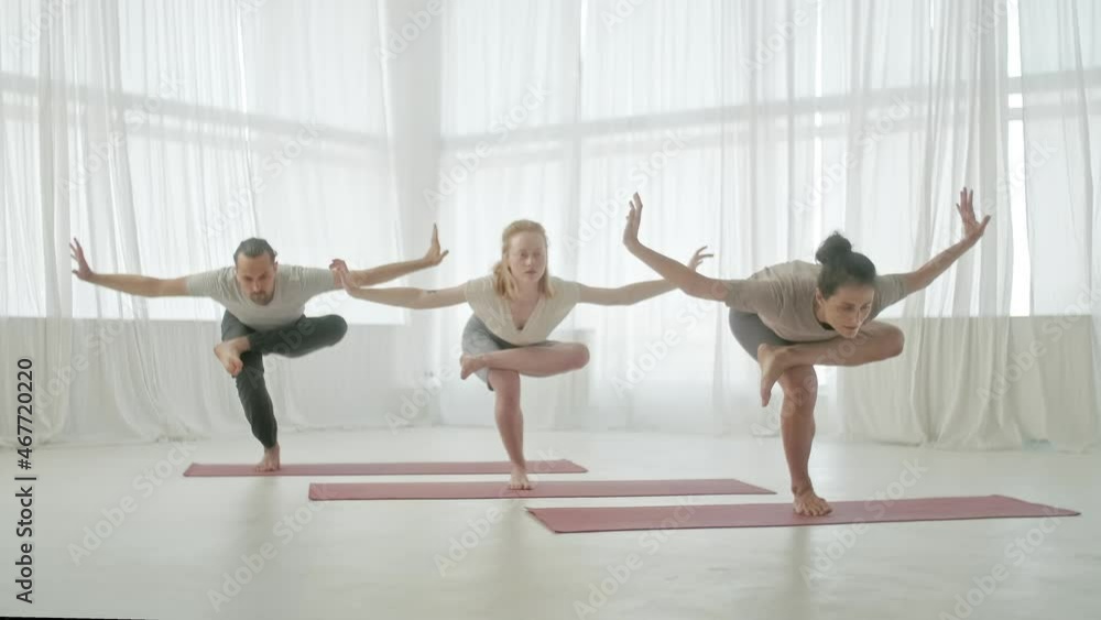Yoga Class Group of Three Women and Man Exercising Healthy Lifestyle in In Bright Studio. People balancing on one leg in in Bright Fitness Studio and Gymnastics Class. Yoga Class Group of Three Women and Man Exercising Healthy Lifestyle in In Bright Studio. People balancing on one leg in in Bright Fitness Studio and Gymnastics Class.