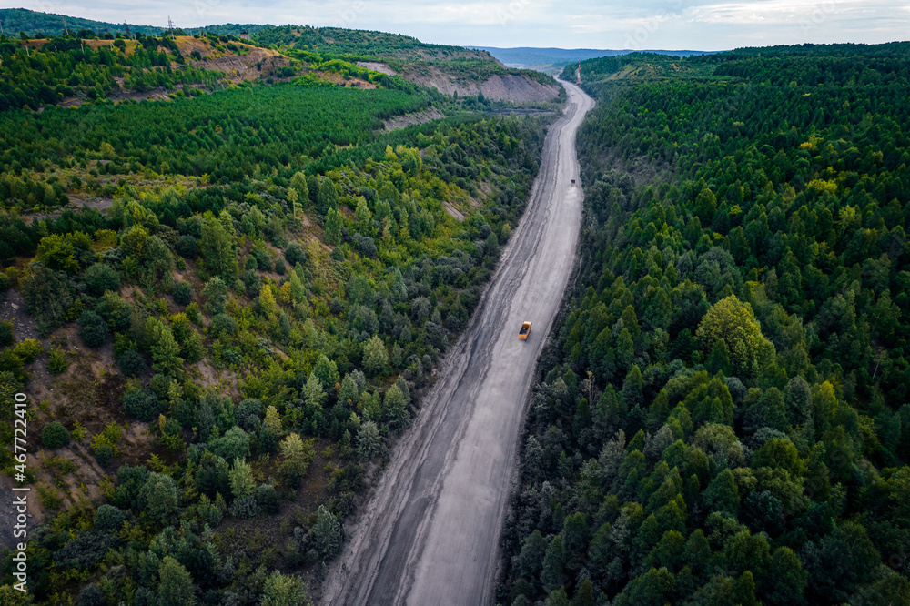 Large yellow truck rides through forest to be loaded into open coal mine