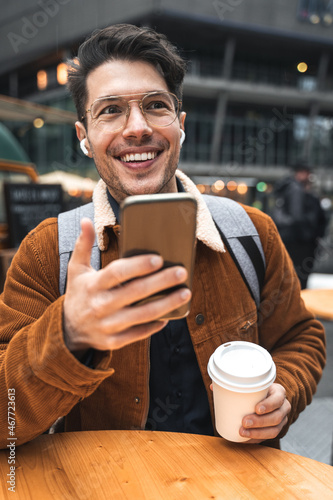 Guy recording voice message while sitting at the street cafeteria with cup of coffee