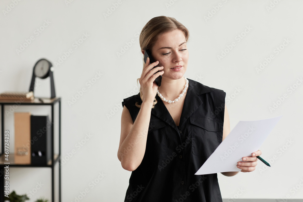 Waist up portrait of blonde successful businesswoman speaking by smartphone in graphic black and white interior, copy space Waist up portrait of blonde successful businesswoman speaking by smartphone in graphic black and white interior, copy space