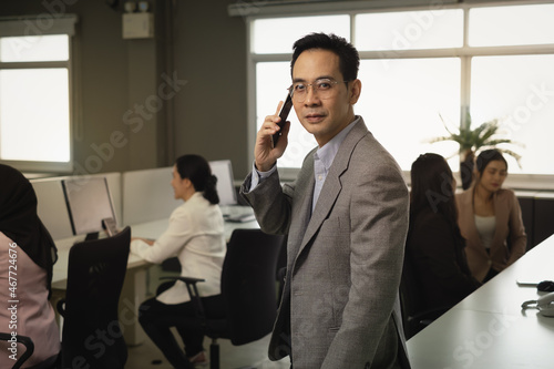 Businessman with glasses and suit holding smartphone observe employees in busy office, representative, posture